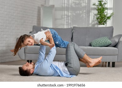 Father Lying On Carpet Floor And Lifting Little Child Girl