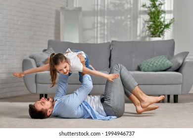 Father Lying On Carpet Floor And Lifting Little Child Girl