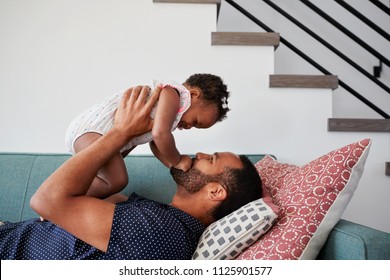 Father Lying On Sofa At Home Lifting Baby Daughter Into Air