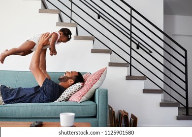 Father Lying On Sofa At Home Lifting Baby Daughter Into Air