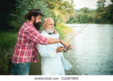 Father and mature son fisherman fishing with a fishing rod on river. Portrait of senior businessman fishing in white suit and bowtie with fishing rod, spinning reel on river.