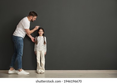 Father measuring daughter's height near black wall indoors, space for text