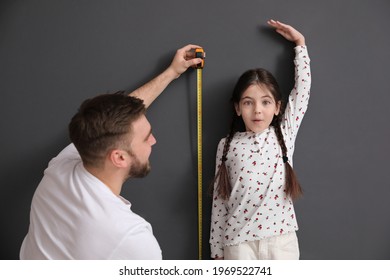 Father measuring daughter's height near black wall