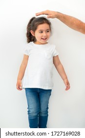 Father Measuring Height Of A Cute Child. Dad Measures The Growth Of Her Child Daughter At A Blank White Wall.