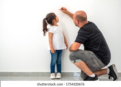 Father Measuring Height Of A Cute Child. Dad Measures The Growth Of Her Child Daughter At A Blank White Wall.