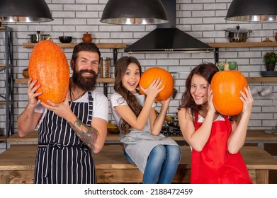 Father Mother And Child In Kitchen. Family Day. Mom Dad And Daughter Wear Aprons.