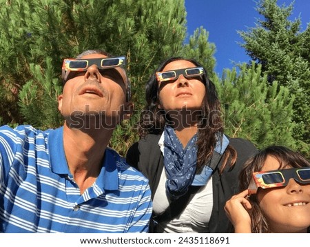 Father, mother and daughter, family viewing solar eclipse with special glasses in a park.