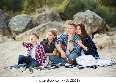 Father Mother Daughter And Son On The Beach. Man And Woman 35-40 Yers Old. Man Plays Guitar.