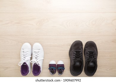 Father, mother and little kid sport shoes on wooden floor background. New family. Closeup. White female, black male and blue baby footwear. Empty place for text.