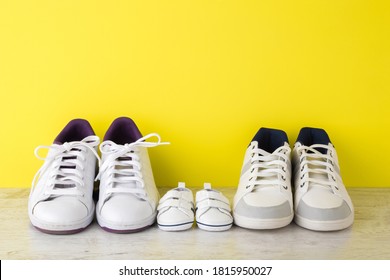 Father, mother and little kid white sport shoes on wooden floor at bright yellow wall. New family. Closeup.