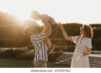 Father, mother, and son are having fun in an old European town. Happy family in the evening. Dad is throwing his little boy up near mom at sunset. - Shutterstock ID 2174767315