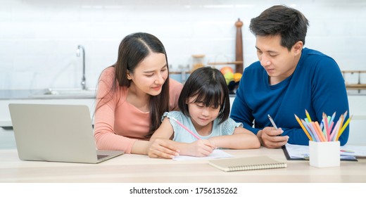 Father And Mother Teaching Children To Do Their Homework At Home. Happy Asian Family Using The Laptop Together At Home. Young Asian Family Parents Helping Daughter Drawing At Home