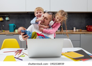 Father with a newborn baby in arms working from home during quarantine and closed school. coronavirus outbreak. Young businessman freelancer works on laptop with children playing around.
