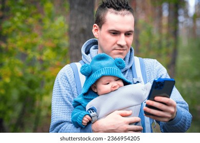 Father and newborn baby in a sling in the autumn forest, man with mobile phone. Happy family. - Shutterstock ID 2366954205