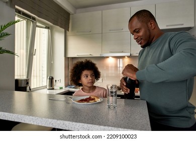 Father Opening Bottle With Cola For His Little Son On Lunch Or Dinner With Pizza At Table At Home Kitchen. Unhealthy Eating. Young Black Family Lifestyle And Relationship. Fatherhood And Parenting