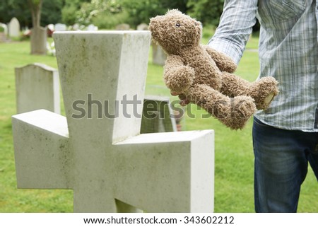 Father Placing Teddy Bear On Child's Grave In Cemetery