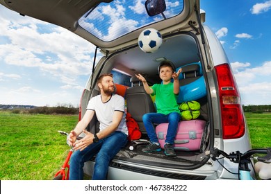 Father Playing Ball With Son Sitting In Car Boot