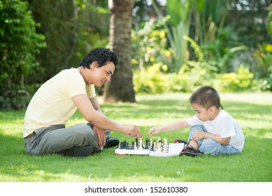 A Father Playing Chess With His Little Son Outside