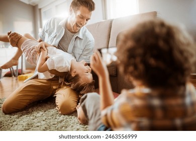 Father playing with daughter while being photographed by son at home - Powered by Shutterstock