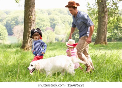 Father Playing Exciting Adventure Game With Children And Dog In Summer Field