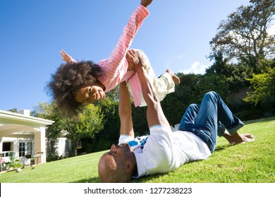 Father playing game lying on grass lifting daughter in air