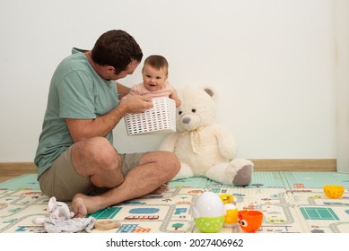 Father Playing With His Baby Daughter At Home. Father Lifting Up His Baby In A Toy Box While Laughing. 