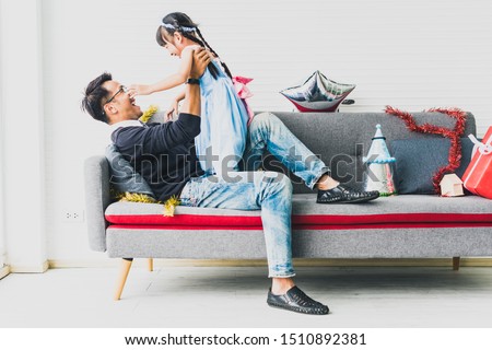 Father playing with his daughter on the sofa in the living room, decorated with ornaments of Christmas and New Year's Day.