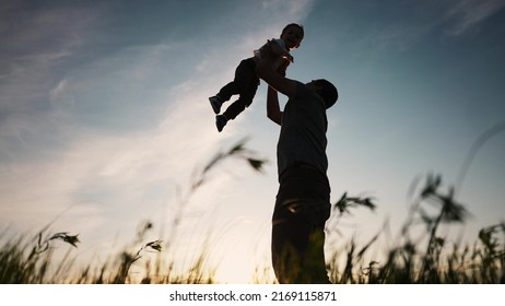 Father Playing With Son In The Park. Happy Family Kid Dream Concept. Father Throws Baby Up Silhouette In Summer At Sunset. Parent And Child Play Lifestyle Toss Up Silhouette Outdoors In The Park