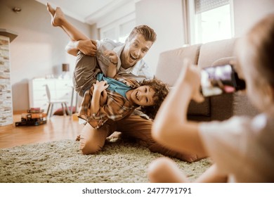 Father playing with son while being photographed by daughter at home - Powered by Shutterstock