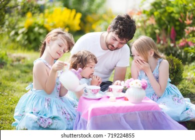 Father playing tea party game with his three adorable daughters. Having many children  caring single father.  Beautiful decorated tea party outdoors. male babysitter, sitter, childminder, sitter-in - Powered by Shutterstock
