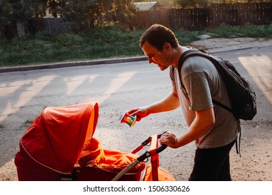 The Father Plays With The Baby In A Pram. Dad Shakes The Rattle.