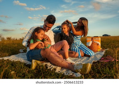 The father plays with his daughter while the mother fixes her other daughter's hair, the family spends quality time outside - Powered by Shutterstock