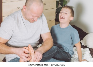 Father plays with his son 7-10 sitting on floor. Dad tickles kids feet. Family having fun
