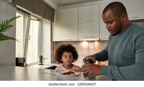 Father Pouring Cola From Bottle In Glass Of Little Son On Lunch Or Dinner With Pizza At Table At Home Kitchen. Unhealthy Eating. Young Black Family Lifestyle And Relationship. Fatherhood And Parenting