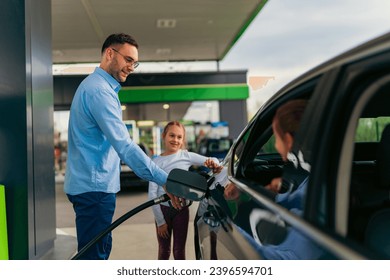 The father pours fuel into the car while his daughter watches him and keeps him company, younger daughter is sitting in the car