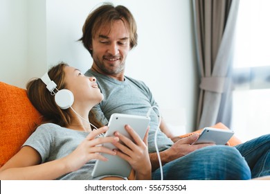 Father and pre teen daughter playing on tablet together on couch in room at home. Good parent and child relations.