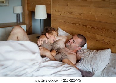Father and preschool son playing and tickling in bed in the morning. Dad with child waking up with positive emotions, spending time together.