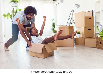Father push cute little daughter sitting inside of carton box having fun riding in living room. Loan mortgage, housing improvement concept. Cheerful happy african family enjoy relocation day. - Powered by Shutterstock