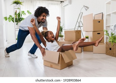 Father push cute little daughter sitting inside of carton box having fun riding in living room. Loan mortgage, housing improvement concept. Cheerful happy african family enjoy relocation day.