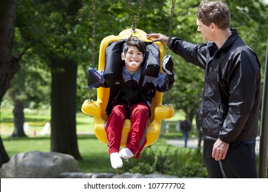 Father Pushing Disabled Boy In Special Needs Handicap Swing. Child Has Cerebral Palsy.