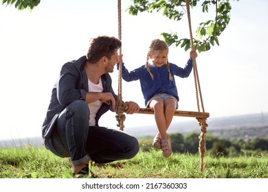 Father Pushing The Little Daughter On A Swing Set