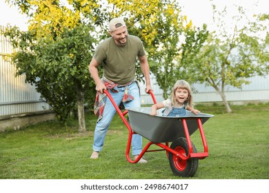 Father pushing wheelbarrow with his daughter outdoors - Powered by Shutterstock