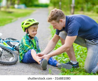 father putting band-aid on young boy's injury who fell off his bicycle.