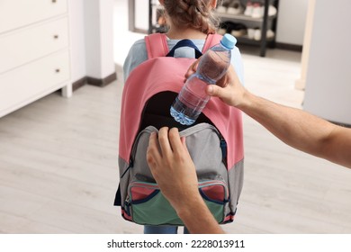 Father putting bottle of water into daughter`s backpack at home, closeup. Preparing to school - Powered by Shutterstock