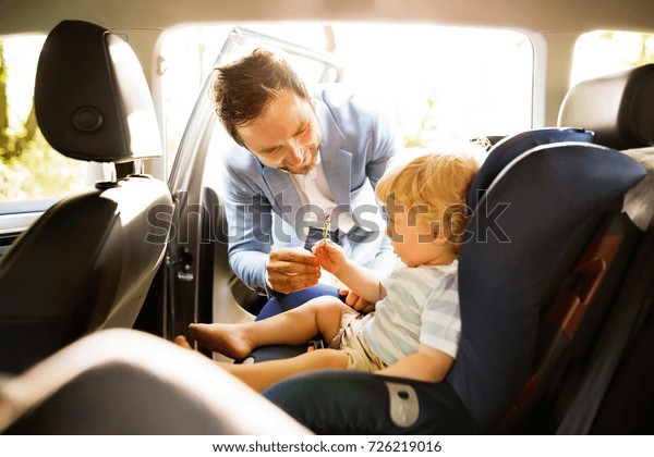 Father putting his son in the\
car.