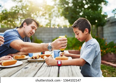 father putting mustard on sons hot dog at family picnic