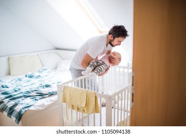 Father Putting A Sleeping Toddler Girl Into Cot At Home.