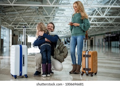 Father Saying Goodbye To His Wife And Daughter At The Airport. He Is Hugging The Child. Their Faces Expressing Joy