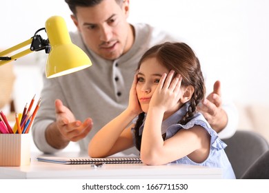 Father scolding his daughter while helping with homework at table indoors - Powered by Shutterstock