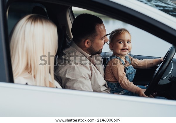 Father Showing His\
Little Daughter How to Drive Car, While Mother Sitting on Passenger\
Seat, Family on Road\
Trip